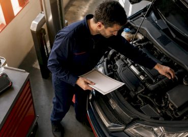 1780487028155_Technician-holding-certificate-near-car-engine-bay Un technicien pose fièrement à côté d’un moteur de voiture, certificat en main.