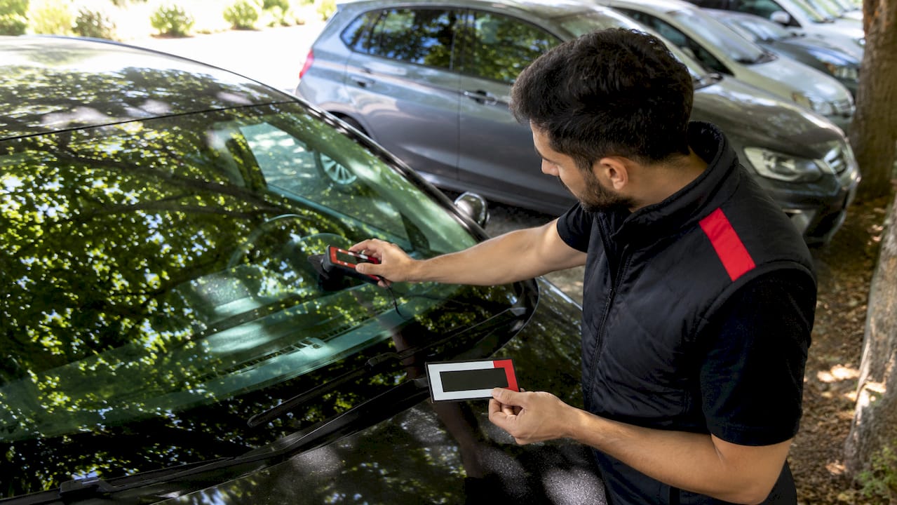 Un technicien contrôle le taux de passage de la lumière à travers une vitre de voiture.