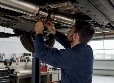 1785882368019_Technicien-posant-un-pot-d-echappement-inox-sous-une-voiture Un professionnel de l’automobile installe un nouvel échappement en inox sous le châssis d’une voiture.